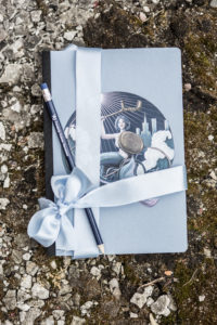 zestaw niebieski notes z syrenką na wózku i ołówek z napisem Fundacja Kulawa Warszawa. Wszystko przewiązane błękitna wstążką